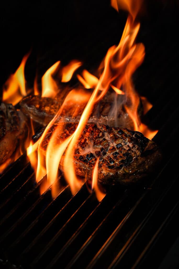 Steaks sur barbecue : Flammes intenses et cuisson parfaite. Steaks de bœuf juteux saisis sur une grille de barbecue. Les flammes orange vives enveloppent la viande dans l'obscurité, créant un contraste dramatique.